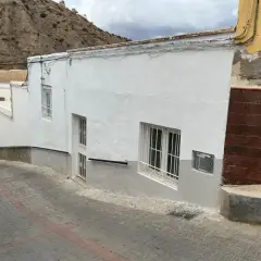 Calle empedrada en un pueblo blanco de Andalucía, con casas encaladas y una ladera rocosa al fondo. Un coche plateado aparcado. Gador, Almería.