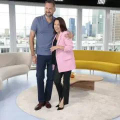 Ewa Drzyzga i Marcin Borowski stoją objęci na tle okien z widokiem na miasto.