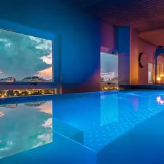 Piscina iluminada con luces azules en un spa de Valencia, con vistas a la ciudad al atardecer.