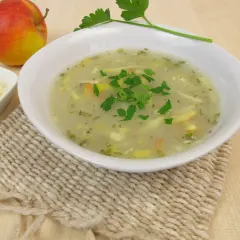 Aromaticzna zupa chrzanowa z chrzanem ze słoika, udekorowana natką pietruszki, obok jabłko i starty ser.