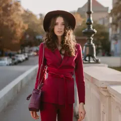 Elegancka kobieta w amarantowym garniturze i kapeluszu spaceruje po moście.