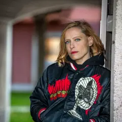 Wanda Bendjelloul, med blå ögon och rött läppstift, bär en svart jacka med en fläkt-design.