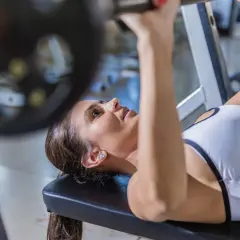Kvinna utför incline press med skivstång på ett gym.
