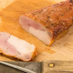 Soczysta polędwica pieczona na kanapki, pokrojona na desce, gotowa do podania. Obok nóż i widelec.
