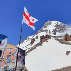 Kolorowy budynek i gruzińska flaga na tle ośnieżonych szczytów. Kazbek wysokość robi wrażenie.