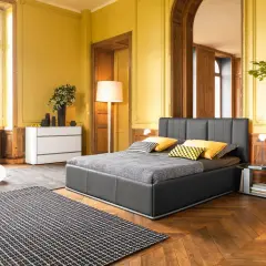 Camera da letto classica con pareti giallo ocra, letto grigio, tappeto a scacchi e arredi in legno.