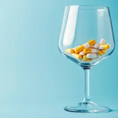 Ein Weinglas gefüllt mit Kapseln, die an Antibiotika erinnern. Vorsicht bei der Einnahme von Medikamenten und Alkohol.