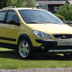 Żółty Hyundai Getz Cross zaparkowany na trawie obok torby golfowej.