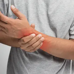 Uomo con dolore al polso, evidenziato da un'area rossa. Potrebbe indicare una distorsione al polso o un'altra infiammazione.