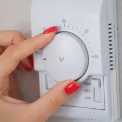 Mano ajustando el termostato para la temperatura calefacción noche. Se ve el dial con grados y el selector de potencia.