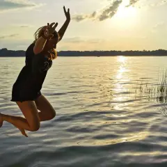 Dziewczyna skacze do wody o zachodzie słońca. Jej ciało w powietrzu, radość i wolność. Boże ciało w pełni.