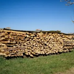 Ein großer Stapel gespaltenes Holz liegt im Freien, teilweise mit einer Plane zum holz abdecken oder nicht.