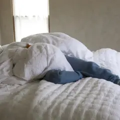 A person sleeps under white linen sheets, a cozy scene that hints at how to wash linen sheets for ultimate comfort.