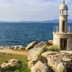 Faro de piedra en Punta Moreiras, con el mar azul de fondo y rocas en primer plano.