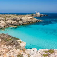 Scogliera rocciosa con mare cristallino e un faro in lontananza, un angolo di paradiso tra le favignana spiagge.