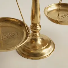 Złota waga szalkowa z napisami "RYZYKO" i "ZYSK". Emitent kto to? To pytanie o równowagę między ryzykiem a zyskiem.