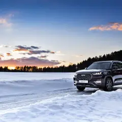 Un SUV noir roule sur une route enneigée au coucher du soleil. La loi montagne impose des équipements pour affronter ces conditions.