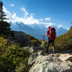 Randonneur avec sac à dos rouge, bâtons de marche, sur un sentier rocheux. Montagnes enneigées en arrière-plan. Combien de jours de marche pour atteindre ce sommet ? gr5.