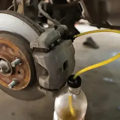 Bleeding car brakes with the cap off the bleed screw, using a yellow tube to drain fluid into a bottle.
