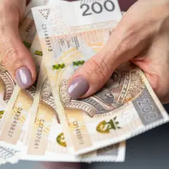 Dłonie trzymające stos banknotów 200 zł. Czy emerytura kapitałowa jest korzystna? Pieniądze to klucz do przyszłości.