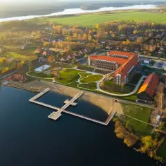 Widok z lotu ptaka na kompleks Lake Hill Mazury z jeziorem, plażą, molo i budynkami w jesiennej scenerii.