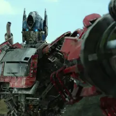 Optimus Prime, przywódca Autobotów, z niebieskimi oczami i płonącą bronią, gotowy do walki.