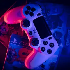 Biały kontroler PlayStation na pudełkach gier: LEGO Jurassic World i Crash Bandicoot. To wersja gry pudełkowa, którą można postawić na półce.