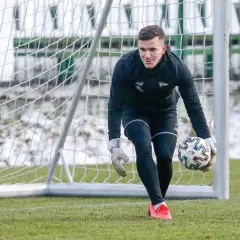 Młody bramkarz piłkarski w czarnym stroju z rękawicami na dłoniach trzyma piłkę, gotowy do akcji.