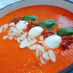 Aksamitna zupa z pieczonej papryki, ozdobiona kulkami mozzarelli, suszonymi pomidorami, płatkami migdałów i listkami bazylii.