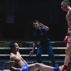 Domare stoppar en match i muy thai. En fighter ligger på mattan, den andra står redo.