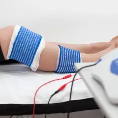 Elektrody podłączone do urządzenia rehabilitacyjnego przy nodze, gdzie widoczna jest kość piszczelowa.