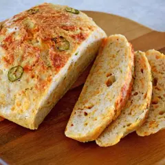 Chleb z serem i papryczką jalapeno, pokrojony na kromki, leży na drewnianej desce.