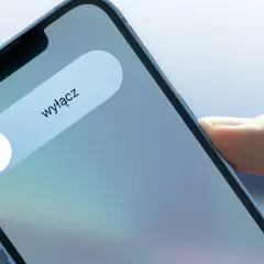 Dłoń trzyma iPhone'a z widocznym suwakiem "wyłącz" i ikoną zasilania.