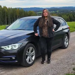 Kvinna vid en svart BMW kombi i svensk landsbygd. Kanske ett bmw b47 problem som gör att hon stannat här.