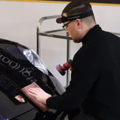 Man polerar en svart Porsche efter lackering med en polermaskin och mikrofiberduk.