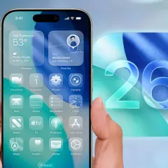 Dłoń trzyma iPhone'a z widokiem na ekran główny, prezentującym widgety i ikony aplikacji. Obok widnieje duży numer 26, symbolizujący najnowszy iOS.