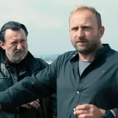 Dwóch mężczyzn na dachu, jeden w skórzanej kurtce, drugi w czarnej koszuli. Scena z jednego z juliusz machulski filmów.