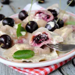 Pyszne pierogi z czereśniami, polane śmietaną, ozdobione świeżymi owocami i listkami mięty. Idealne na letni deser.