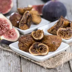 Des figues fraîches et des figues séchées au four sur des assiettes blanches, posées sur du bois rustique.