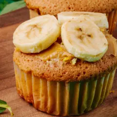 Pyszne muffinki bananowe fit z masłem orzechowym i plasterkami banana na drewnianej desce.