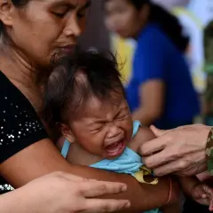 Płacz dziecka podczas szczepień na Filipinach. Matka tuli niemowlę, gdy personel medyczny przygotowuje się do podania szczepionki.