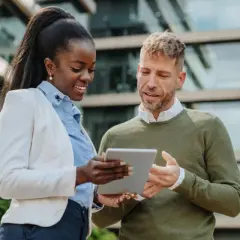 Two professionals discuss their MPA online program on a tablet outside a modern building.