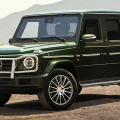 Un imponente Mercedes-Benz verde oscuro, el mejor Mercedes del mundo, se detiene en un camino polvoriento con montañas al fondo.