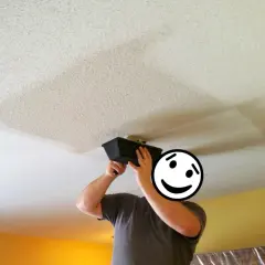 Person applying joint compound to a ceiling, a step in removing popcorn ceiling texture.