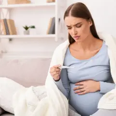 Donna incinta preoccupata guarda il termometro, avvolta in una coperta. La febbre in gravidanza è un sintomo da non sottovalutare.
