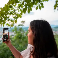 Kobieta robi zdjęcie telefonem. Aby uzyskać czysty kadr, pamiętaj, jak wyczyścić obiektyw w telefonie.
