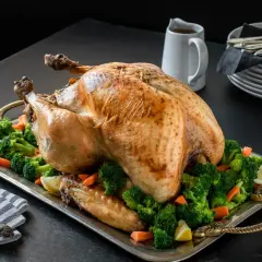 Un jugoso pavo relleno al horno, adornado con brócoli y zanahorias, listo para la celebración.