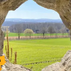 Ein Urlaub am Niederrhein durch ein steinernes Fenster: Grüne Felder, Bäume und ein blauer Himmel.
