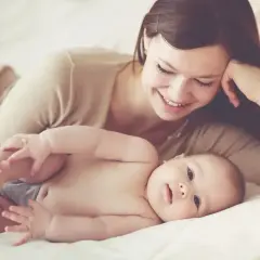 Uśmiechnięta mama na urlopie macierzyńskim bawi się nóżkami swojego dziecka.