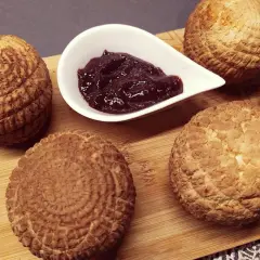 Cztery okrągłe serki do wędzenia, każdy z charakterystycznym wzorem, obok miseczki z konfiturą.